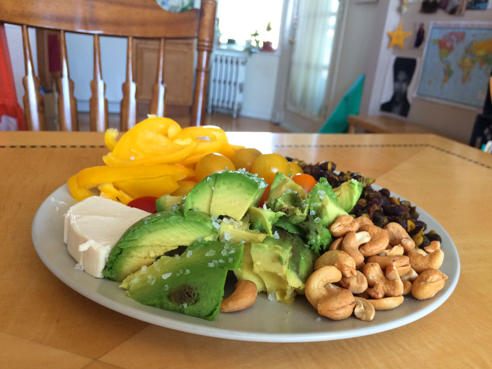 a classic menstruation plate plate on a kitchen table with fresh cheese, sliced yellow peppers and avocado, cashews, sweet grape tomatoes, and black beans
